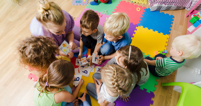 Overhead shot of a group of children all gathered in a circle playing with letter cards