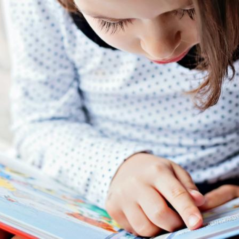 Young girl sat down reading a book tracing her finger across the page