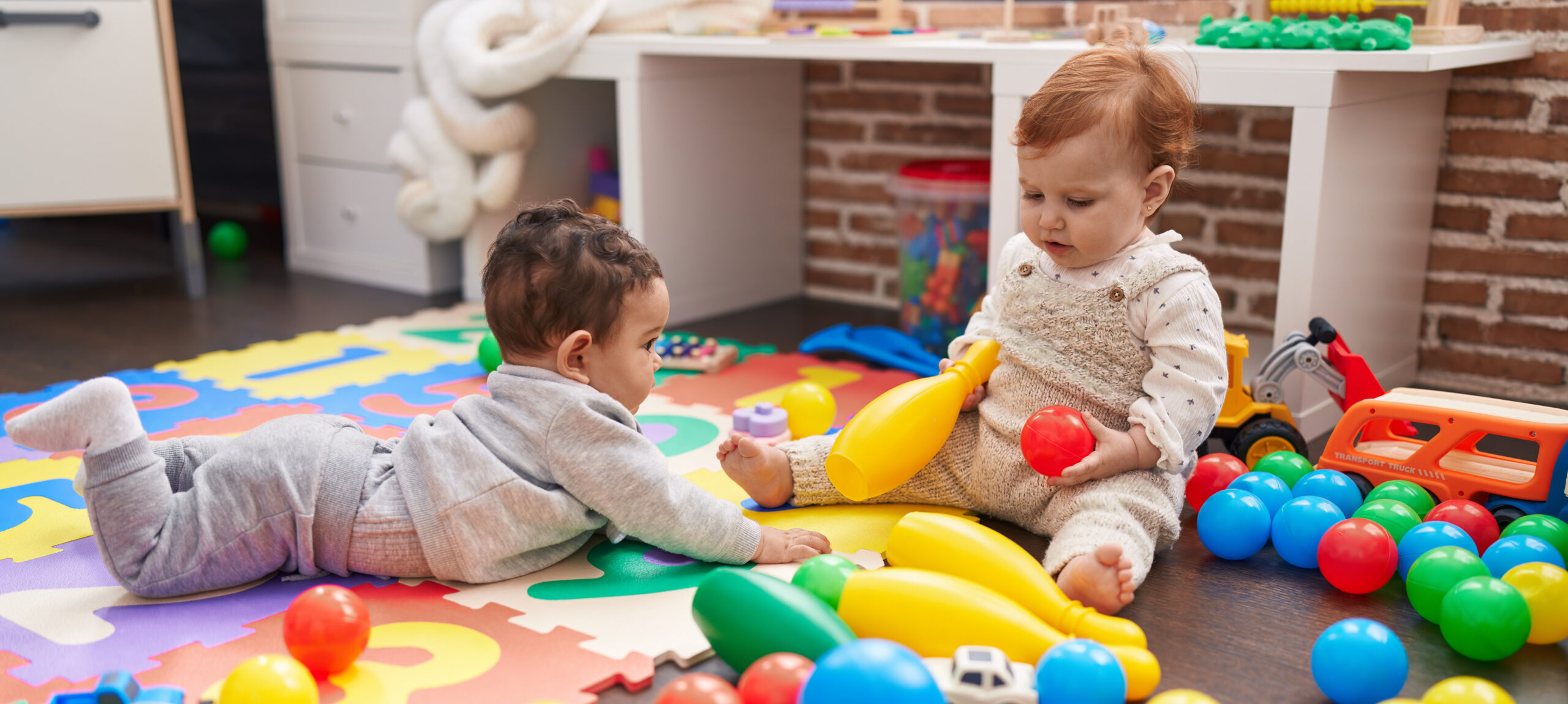 Babies on the floor playing with brightly-coloured toys