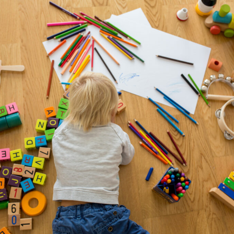 Aerial shot of a little boy lining on the floor surrounded by colouring pencils and wooden blocks drawing on paper