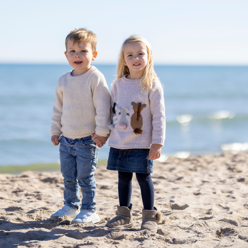 Little boy and girl stood on a beach in front of the sea holding hands and smiling at the camera