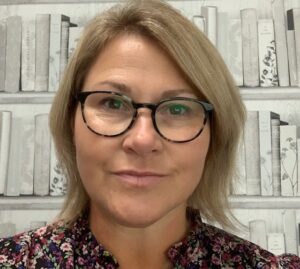 A close up photograph of Emma, a member of staff, smiling. She has short blonde hair and black glasses.