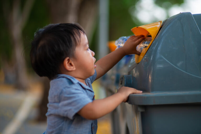 young boy in blur shirt with black hair puts rubbish into a bin