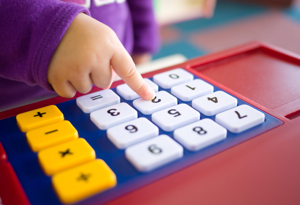 child's hand pushing white buttons on a play calculator or till