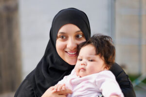 Mother wearing a black hijab smiling holding her baby daughter in front of her