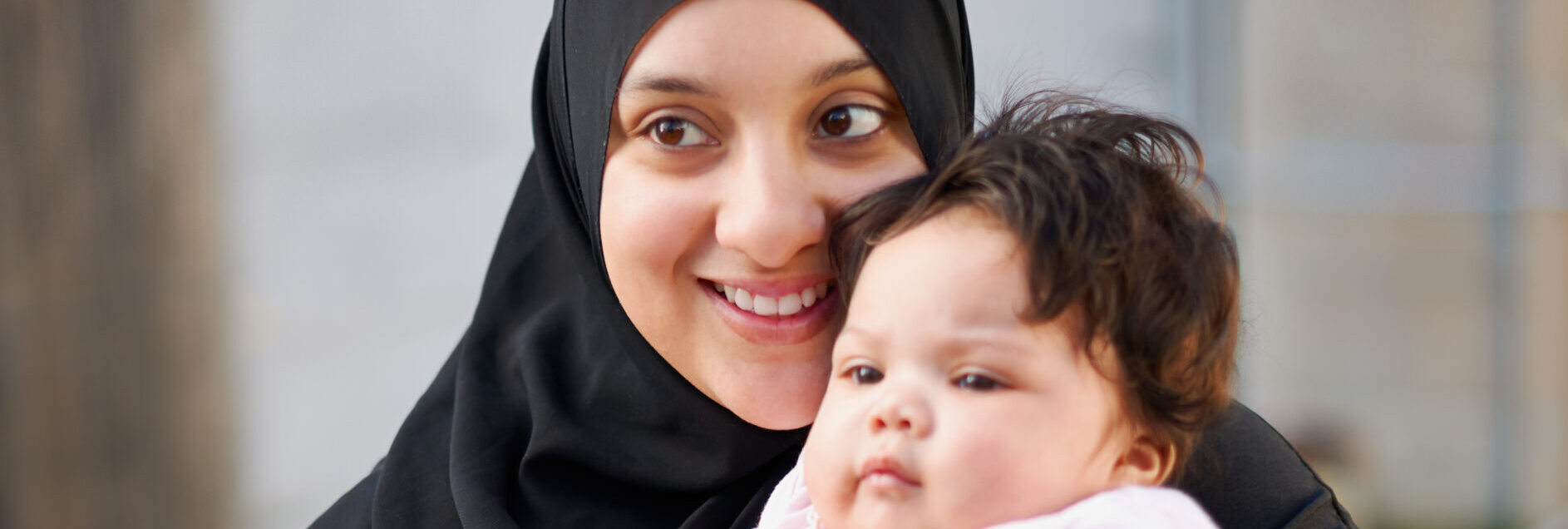 Mother wearing a black hijab smiling holding her baby daughter in front of her