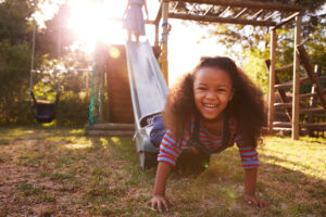 Smiling child climbs off the bottom of an outdoor slide