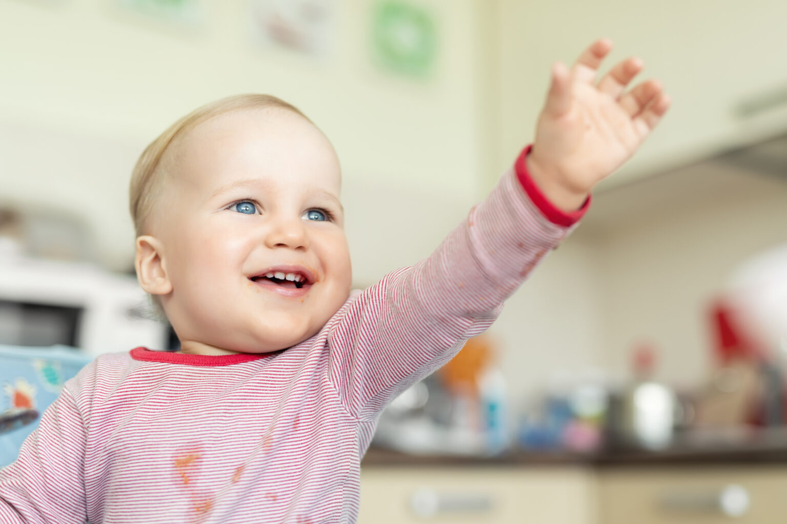 Baby in a red and white stripe t-shirt in a kitchen environment with his hand outstretched